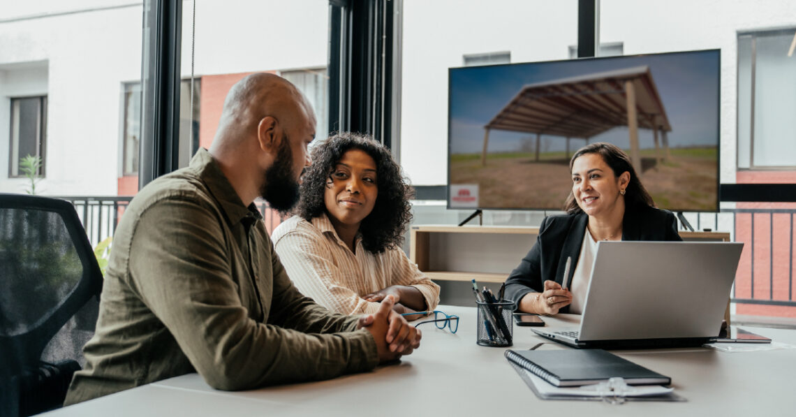This is an image of a couple meeting with a loan officer about pole barn financing. In the background, the pole barn for the loan is pictured.